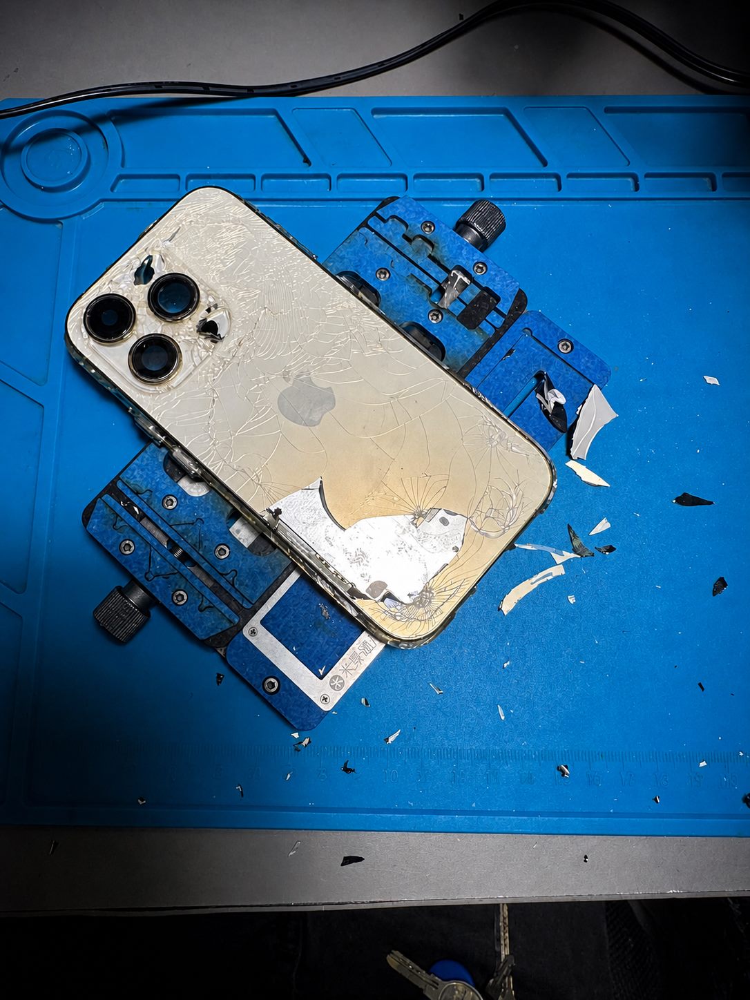 iPhone cu sticla spate spartă, poziționat pe suportul de reparație